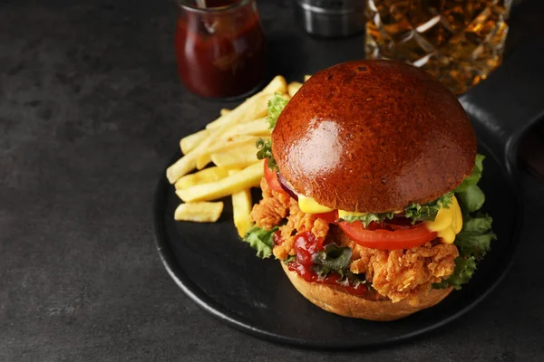 Delicious burger with crispy chicken patty and french fries on black table