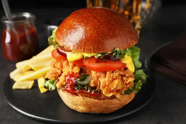 Delicious burger with crispy chicken patty and french fries on black table, closeup