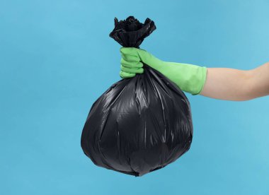 Açık mavi arka planda çöp dolu plastik poşet taşıyan bir kadın, yakın plan. Metin için boşluk