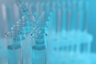 Laboratuvar analizi. Açık mavi arkaplanda pipetten cam test tüpüne sıvı damlatılıyor, yakın plan ve metin için boşluk