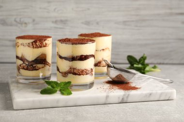 Bardakta nefis tiramisu, nane ve elek hafif desenli masa üzerinde kakao tozu.