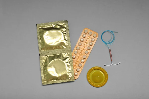 Contraceptive pills, condoms and intrauterine device on light grey background, flat lay. Different birth control methods
