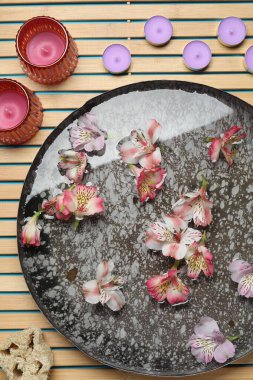 Bir kase çiçekli, mumlu ve lifli tahta hasırın üzerinde, düz bir şekilde yatıyordu. Spa tedavisi