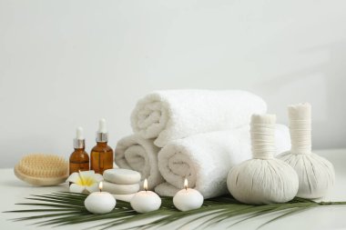 Farklı spa ürünleri içeren kompozisyon, yanan mumlar ve beyaz masa üzerinde plumeria çiçeği