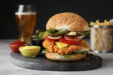 Çıtır tavuk köfteli leziz burger ve gri masada soslar.