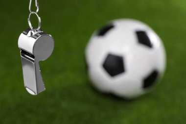 Futbol hakem ekipmanı. Metal düdük ve futbol topu yeşil çimlerin üzerinde, metin için yeri olan yakın plan