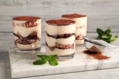 Bardakta nefis tiramisu, nane ve elek hafif desenli masada kakao tozu, yakın plan.