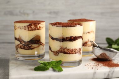 Bardakta nefis tiramisu, nane ve elek, masada kakao tozu, yakın plan.