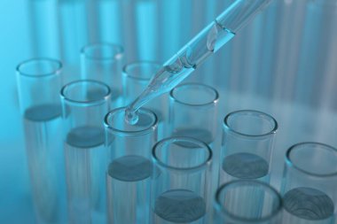 Laboratuvar analizi. Açık mavi arkaplanda pipetten cam test tüpüne sıvı damlatılıyor.