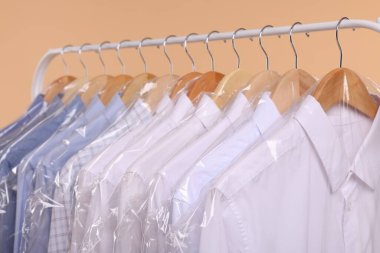 Kuru temizleme servisi. Bej arka planda asılı duran plastik poşetlerde birçok farklı kıyafet, yakın plan.