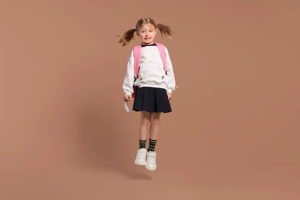 stock image Happy schoolgirl with backpack jumping on brown background