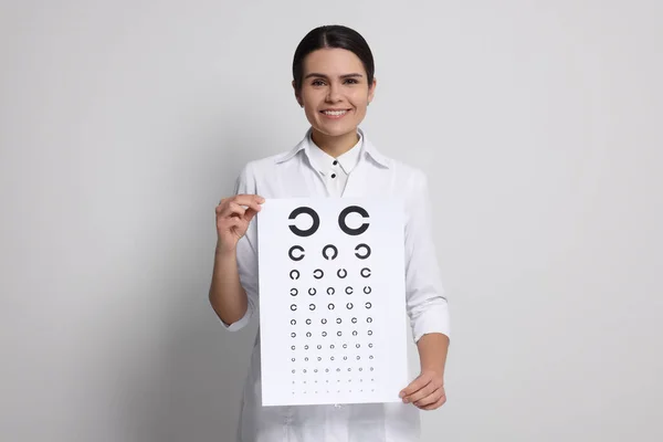Ophthalmologist with vision test chart on light background