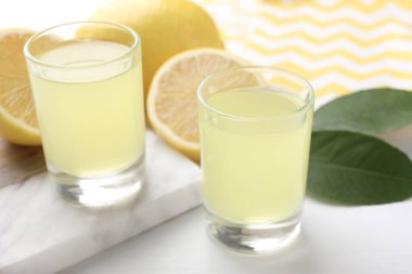 Lezzetli limoncello likörü, limonlar ve yeşil yapraklar beyaz masada, yakın plan.