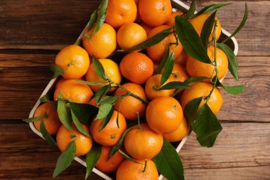 Tahta masanın üstünde yeşil yapraklı taze mandalinalar.