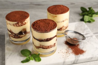 Bardakta nefis tiramisu, nane ve elek, masada kakao tozu, yakın plan.
