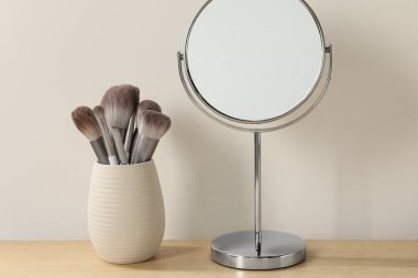 Odadaki ahşap tuvalet masasında ayna ve makyaj fırçaları.