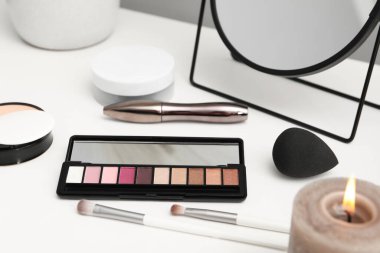 Ayna, kozmetik ürünleri ve tuvalet masasında yanan mum.