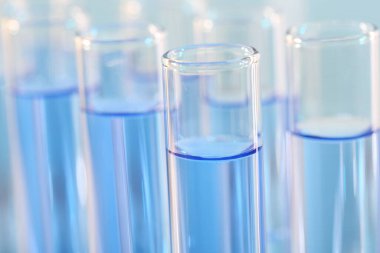 Laboratuvar analizi. Bulanık arkaplanda açık mavi sıvı bulunan birçok cam test tüpü, yakın plan