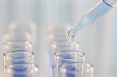 Laboratuvar analizi. Pipetten açık mavi sıvıyı bulanık arkaplanda cam test tüpüne damlatarak, yakın plan