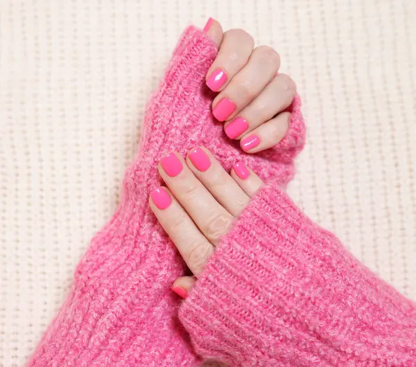Woman showing her manicured hands with pink nail polish on knitted blanket, top view