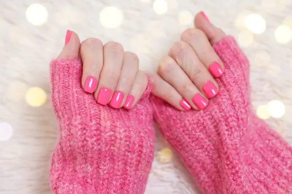 Woman showing her manicured hands with pink nail polish on faux fur mat, closeup. Bokeh effect