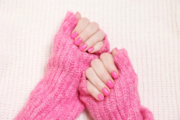 Woman showing her manicured hands with pink nail polish on knitted blanket, top view