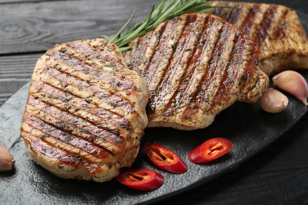 Delicious grilled pork steaks with spices on wooden table, closeup