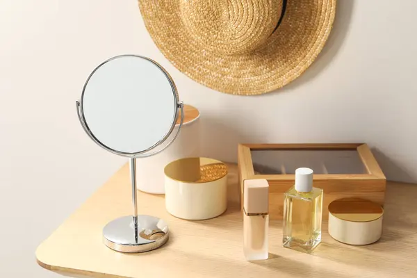 Mirror, perfume and makeup products on dressing table in room