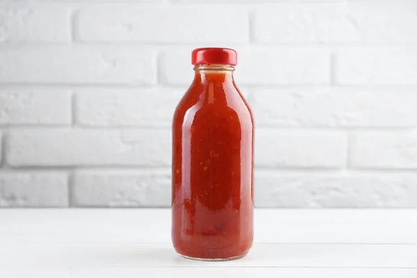 Spicy chili sauce in bottle on white wooden table