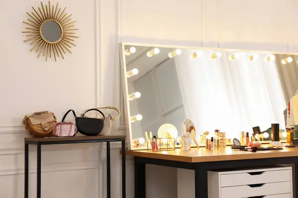 Makeup room. Stylish mirror with light bulbs, beauty products and bags on wooden table