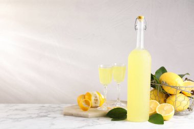 Lezzetli limoncello likörü, limonlar ve yeşil yapraklar beyaz mermer masa üzerinde, metin için boşluk