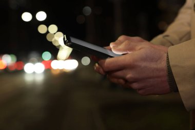 Gece caddesinde akıllı telefon kullanan bir adam, yakın plan. Metin için boşluk
