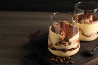 Bardakta nefis tiramisu, ahşap masada kaşık ve kahve çekirdekleri, yakın plan. Metin için boşluk