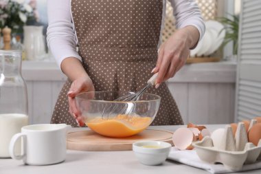 Kadın kasede yumurta çırpıyor, kapalı bir masada, yakın plan.