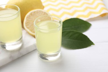 Lezzetli limoncello likörü, limonlar ve yeşil yapraklar beyaz masada, yakın plan. Metin için boşluk