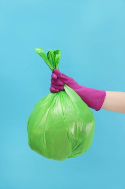 Açık mavi arka planda çöp dolu plastik poşet taşıyan kadın, yakın plan.