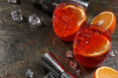 Aperol sprey kokteyli, buz küpleri ve gri desenli masada portakal dilimleri, metin için boşluk.