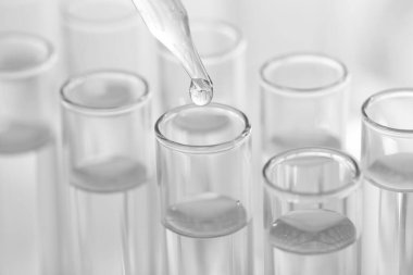 Laboratuvar analizi. Bulanık arkaplanda, pipetten cam test tüpüne sıvı damlıyor.