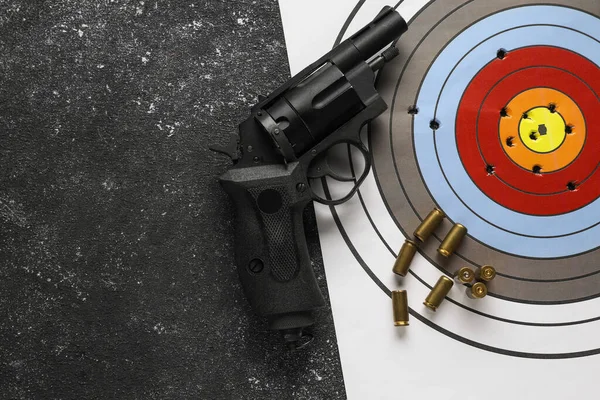 Shooting target, handgun and bullets on dark gray table, top view. Space for text