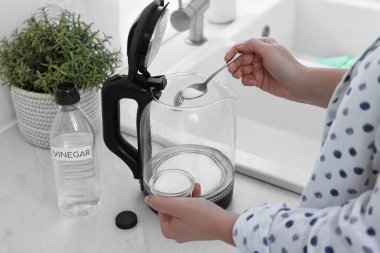 Mutfaktaki su ısıtıcısına kabartma tozu ekleyen kadın, yakın plan.