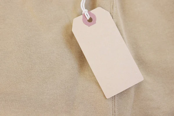 Cardboard tag on beige garment, top view. Space for text