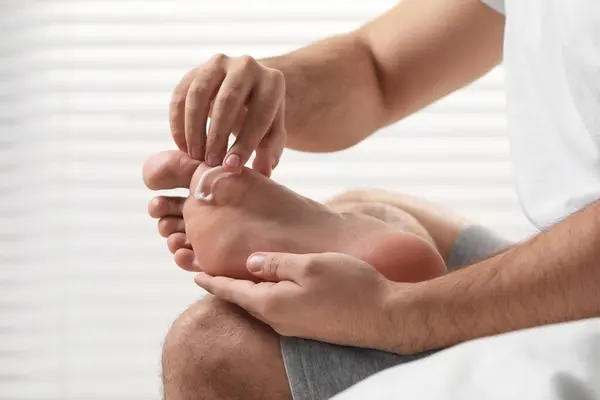 Man with dry skin applying cream onto his foot on light background, closeup