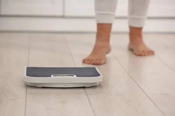 Menopause, weight gain. Woman standing on floor indoors, focus on scales