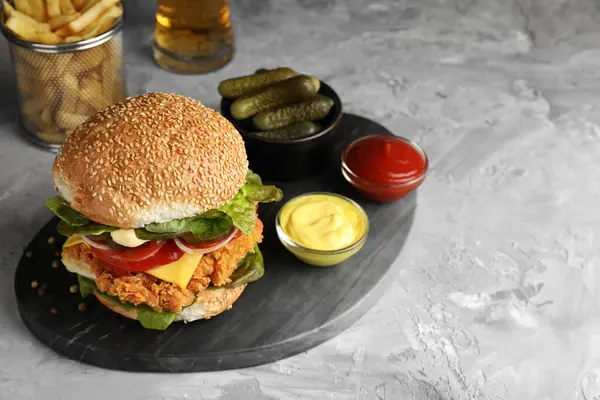 Delicious burger with crispy chicken patty and sauces on grey table