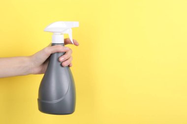 Sarı arka planda plastik sprey şişesi tutan kadın, yakın plan. Metin için boşluk