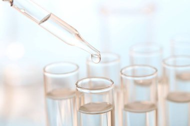 Laboratuvar analizi. Bulanık arkaplanda, pipetten cam test tüpüne sıvı damlıyor.