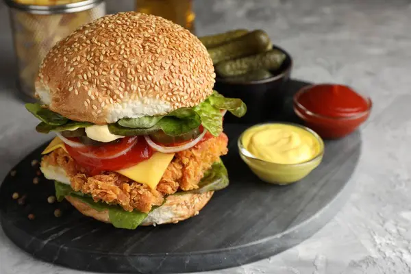Delicious burger with crispy chicken patty and sauces on grey table, closeup