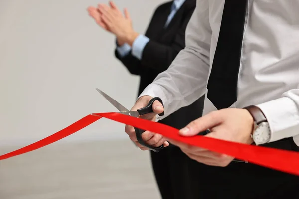 Man cutting red ribbon with scissors indoors, closeup