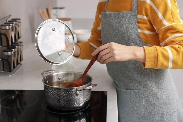 Woman cooking soup on cooktop in kitchen, closeup