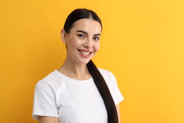 Dişleri temiz, sarı arka planda gülümseyen güzel bir kadın.